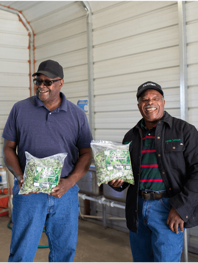 Two men smiling holding a bag of salad